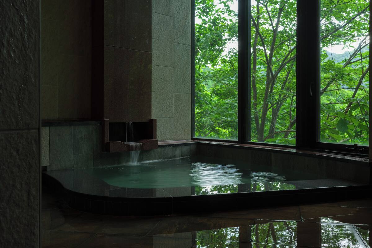 A spa area with a water feature and a view of lush greenery through large windows.