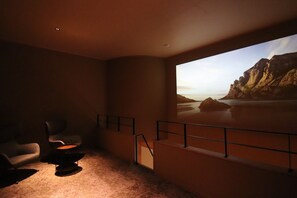 A room with a large screen displaying a scenic view, a seating area with two chairs, and a staircase leading to an upper level. - suigan (Sapporo)
