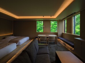 A modern hotel room with a bed, a sofa, a small table, and a view of greenery through the windows. - suigan (Sapporo)