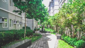 Un chemin bordé de verdure et d’arbres, menant à un bâtiment doté de nombreuses fenêtres et de plusieurs unités de climatisation.