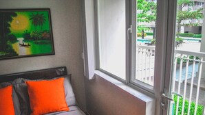Une chambre d’hôtel avec un lit, une fenêtre donnant sur une piscine et un espace verdoyant, et un tableau accroché au mur.