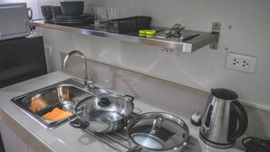 Une cuisine équipée d’un évier en acier inoxydable, de deux casseroles, d’une bouilloire et d’une étagère au-dessus de l’évier où sont rangés divers ustensiles de cuisine.