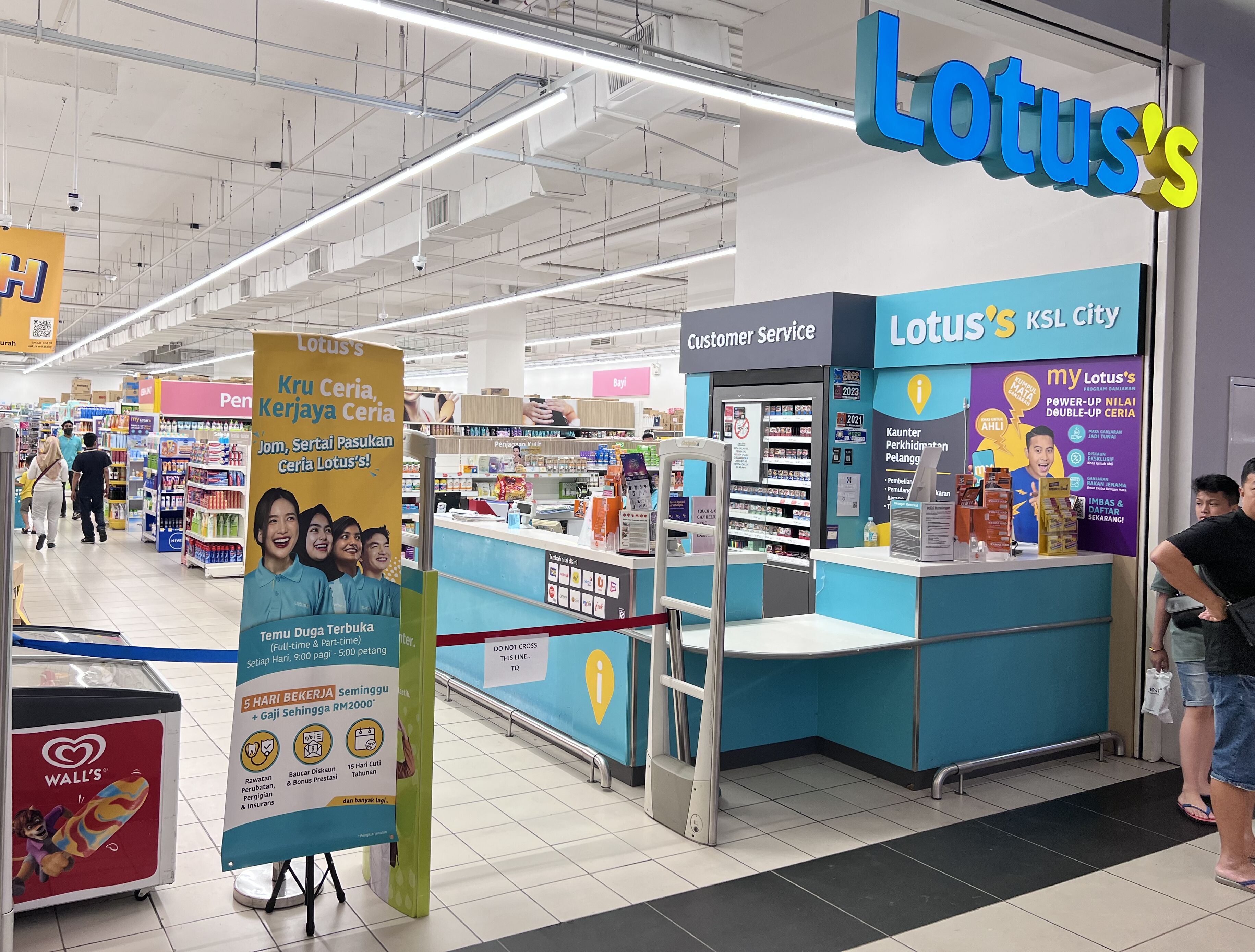 A customer service counter at a Lotus's KSL City store with a blue and white color scheme, a visible sign for customer service, and a promotional banner for Wall's.