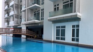 Un bâtiment moderne doté d’une piscine, de balcons avec des garde-corps en verre et d’un pont en bois qui enjambe la piscine.