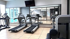 Une salle de sport équipée de tapis de course, de vélos elliptiques et d’un téléviseur fixé au mur.