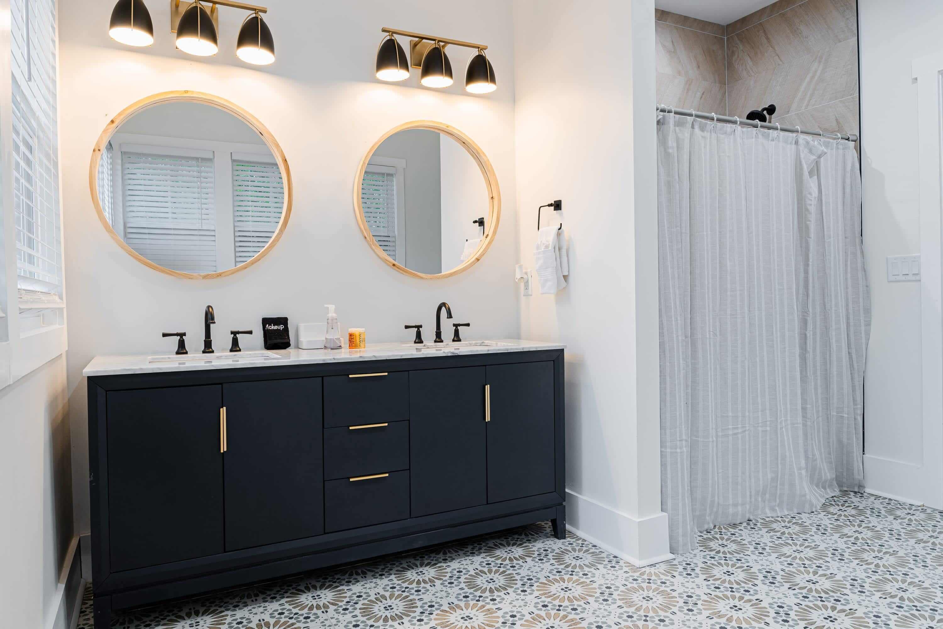 Une salle de bain avec un meuble-lavabo noir, deux miroirs ronds, un rideau de douche et des carreaux de sol à motifs.