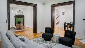 A spacious living room with a grey sofa, two black armchairs, a patterned rug, and a fireplace with a green tiled surround. - Historic Gem in the Heart of Norcross (Norcross)