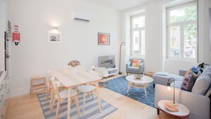 A modern living room with a dining area, a sofa, a TV, and a large window. - Liiiving in Porto - Haven Pool Apartment (Porto)