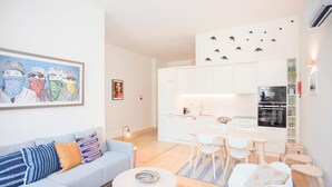 A modern living room with a sofa, coffee table, and a dining area with chairs and a table. - Liiiving in Porto - Haven Pool Apartment (Porto)