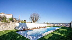 A swimming pool with a clear view of the surrounding landscape, a stone wall, and a tree. - Liiiving in Porto - Haven Pool Apartment (Porto)