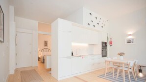 A compact kitchen with white cabinetry, a dining area with a table and chairs, and a small rug on the floor. - Liiiving in Porto - Haven Pool Apartment (Porto)