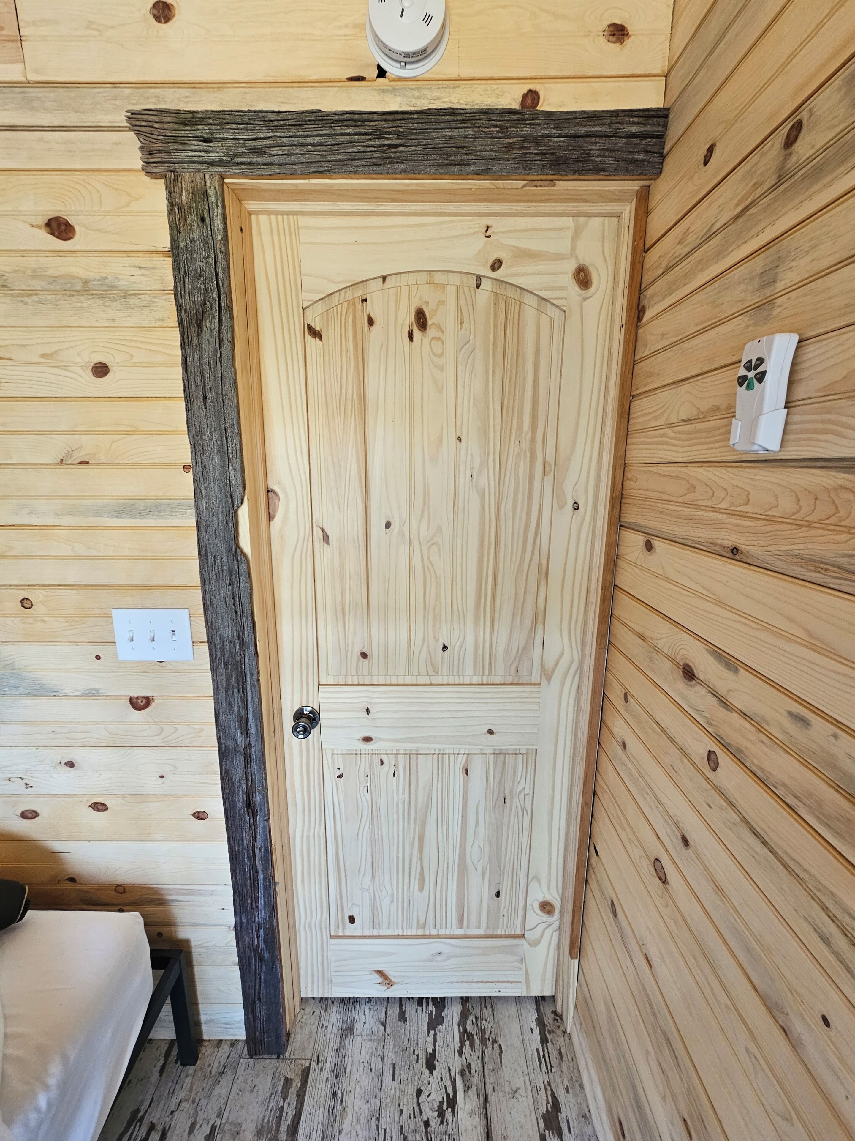 Eine Holztür mit rustikalem Design, ein kleines Fenster darüber und eine Steckdose an der linken Wand.