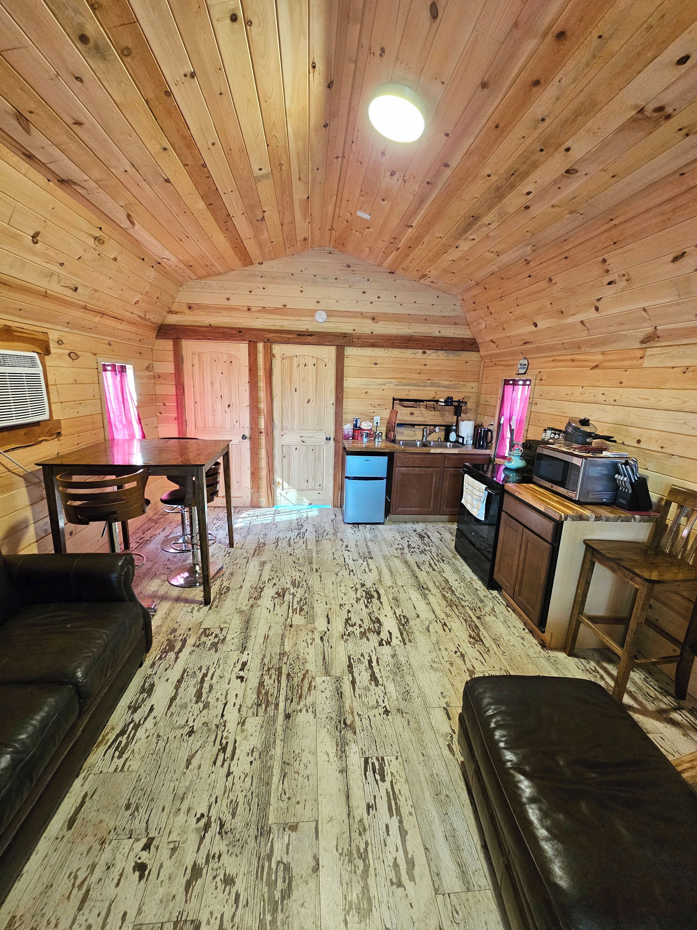A wooden cabin interior with a dining area, kitchen, and seating space.
