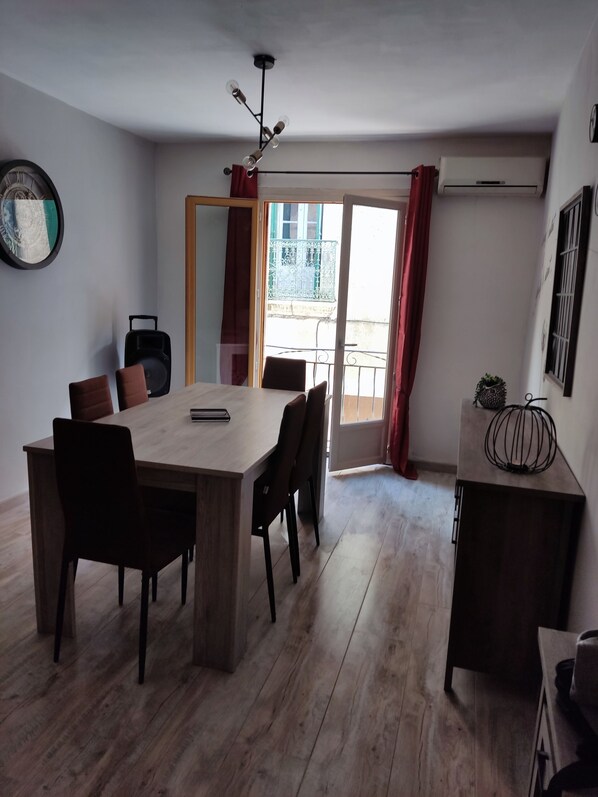 A dining area with a wooden table and chairs, a ceiling light fixture, and a view of the outside balcony through a glass door.