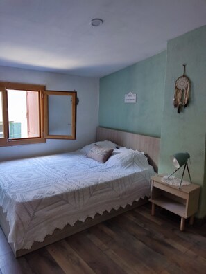 A bedroom with a bed, a bedside table, a lamp, a wall decoration, and a window.