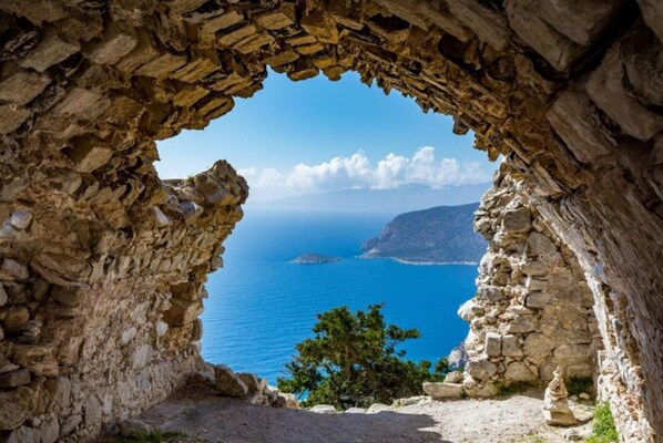 A stone archway leading to a view of the sea and a distant island.
