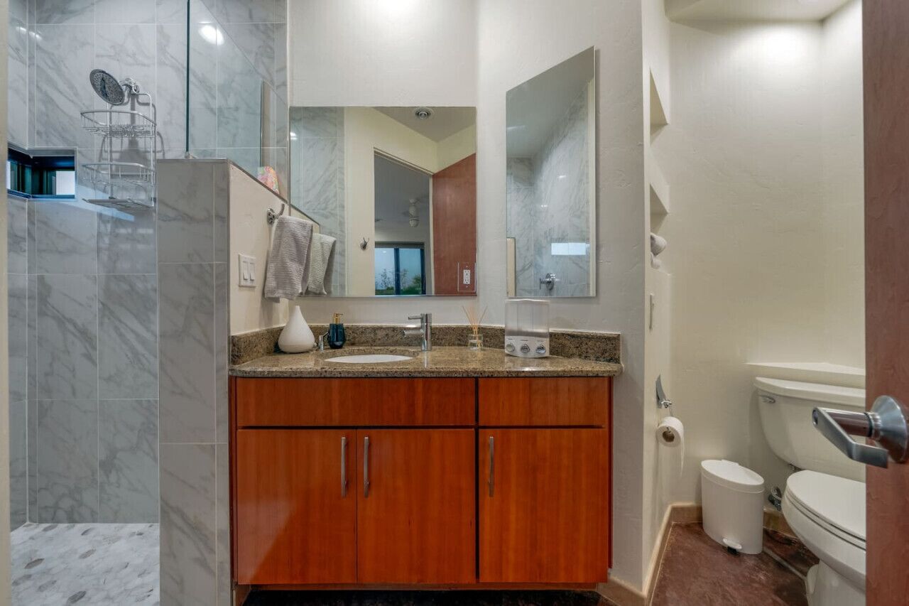 Un bagno moderno con doccia in marmo, mobile bagno in legno e uno specchio grande.