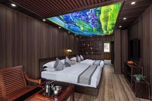 A hotel room with a large bed, a desk with a kettle, and a television.