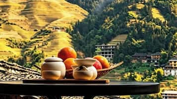 Una mesa con teteras y naranjas en una terraza con vistas a campos escalonados.