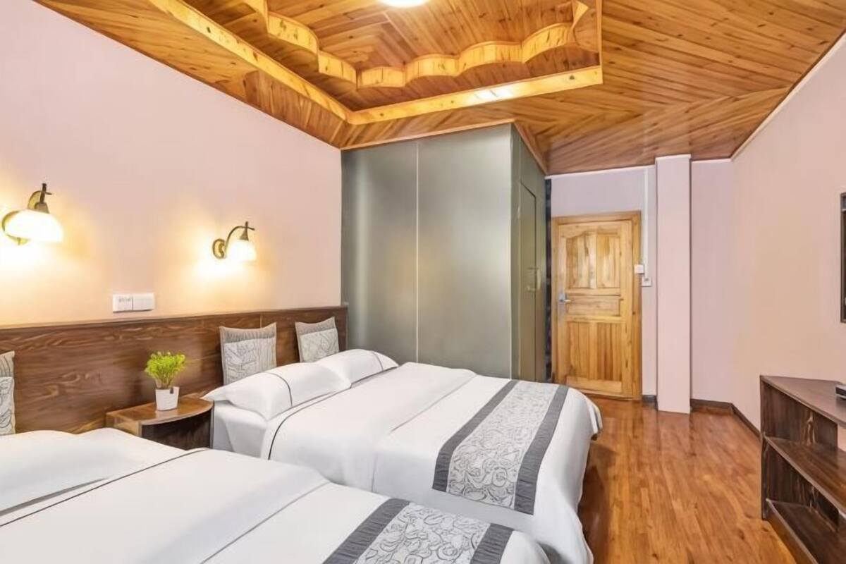 Ein Hotelzimmer mit zwei Betten, Holzboden, Wandlampen, einem kleinen Nachttisch mit Pflanze und einem Kleiderschrank.