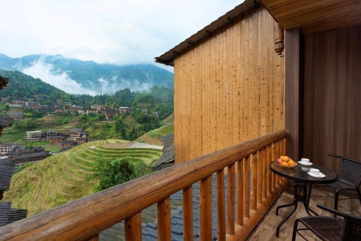 A wooden balcony with a view of terraced fields and mountains.