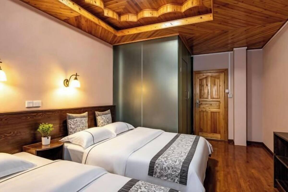 Ein Hotelzimmer mit zwei Betten, Holzbalkendecke, einem Kleiderschrank und Wandleuchten.