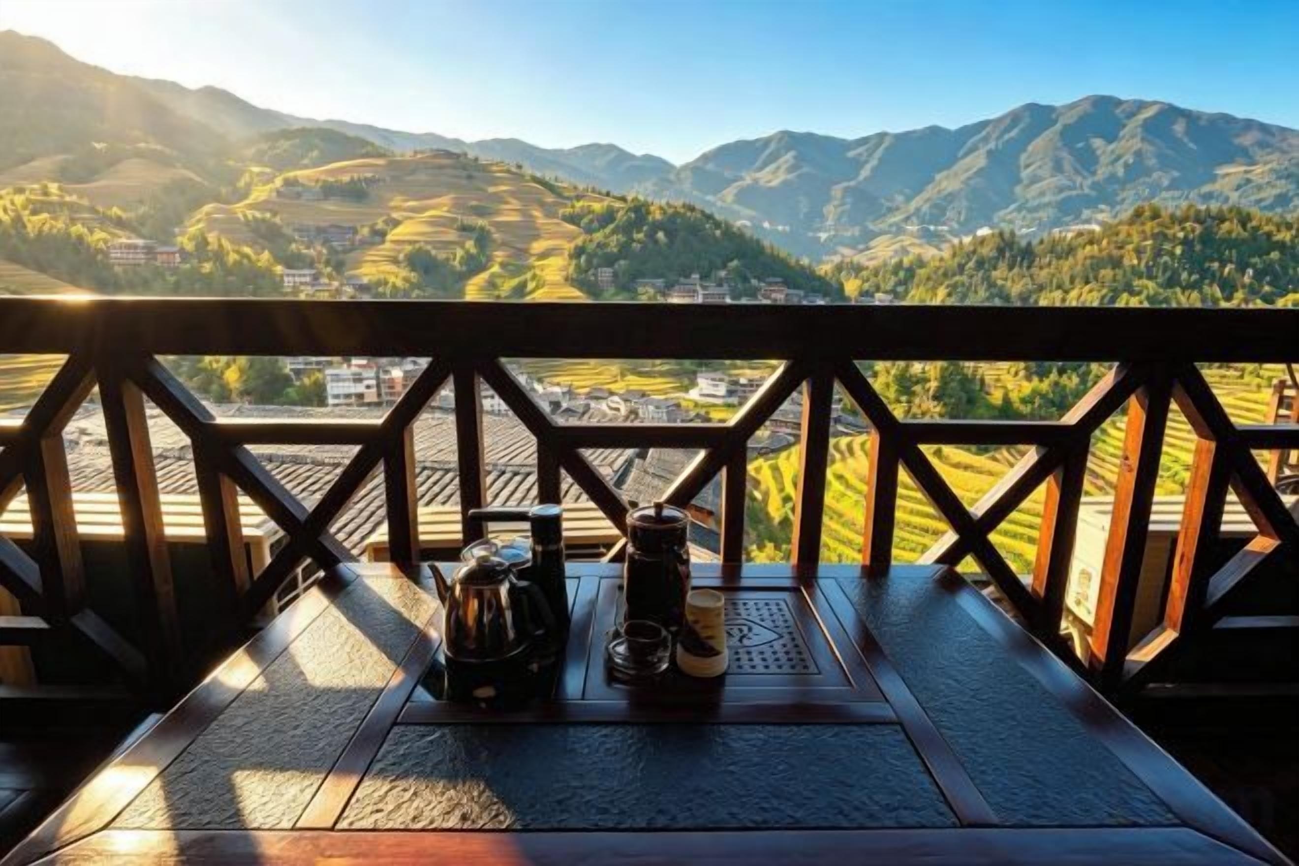 A wooden table with a kettle, cups, and a bottle, overlooking a mountainous landscape.