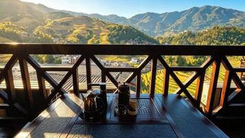 A wooden table with a kettle, cups, and a bottle, overlooking a mountainous landscape.