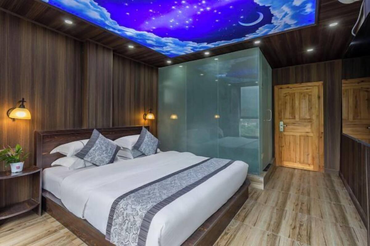 Ein Schlafzimmer mit Bett, Wandgemälde des Nachthimmels, Holzwänden und einer Glasabtrennung.