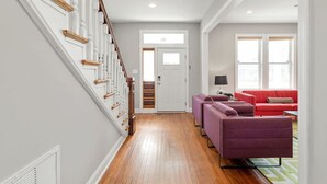 A hallway with a wooden staircase, a red sofa set, and a door leading to another room.
