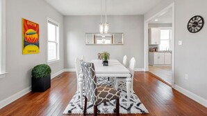 A dining area with a white table, giraffe-patterned chairs, a black potted plant, and a modern chandelier.