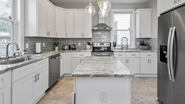 A modern kitchen with white cabinets, a central island, stainless steel appliances, and pendant lighting.