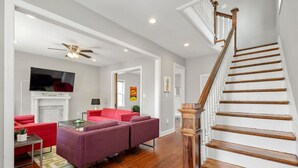 A spacious living room with a red sofa, purple armchairs, and a wooden staircase.