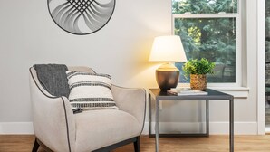 Ein modernes Wohnzimmer mit einem grauen Sessel, einer schwarz-weißen Decke, einem Tisch mit Lampe und einem gewebten Blumentopf.