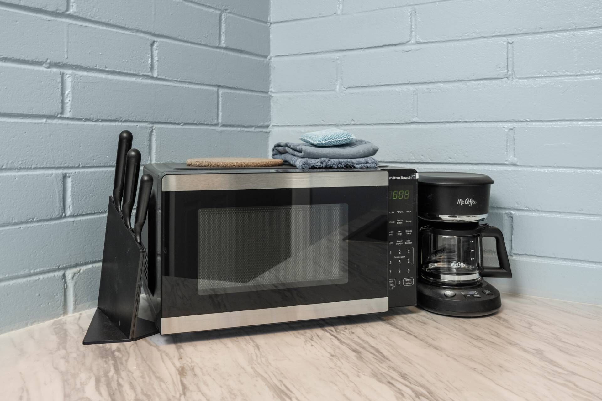 Un four à micro-ondes et une machine à café sont posés sur un plan de travail de cuisine, avec un bloc à couteaux placé à gauche.