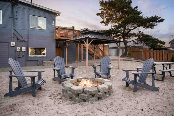 A backyard with a fire pit, four Adirondack chairs, and a wooden deck.
