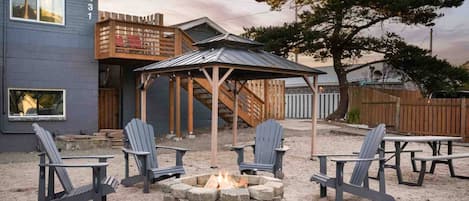 En terrasse med Adirondack-stole, bålsted og en træpergola.