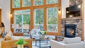 A cozy living room with a stone fireplace, large windows, and comfortable seating. - Spectacular Private Mountain Cabin on 6 Acres, Epic Outdoor, Hot Tub, Game Room, Pond (Rhododendron)
