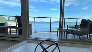 A room with a large sliding glass door leading to a balcony overlooking a body of water. - INN OF THE SEA - Stunning views~ Oceanfront Pool & Hot Tub, Private Dock (Ladysmith)