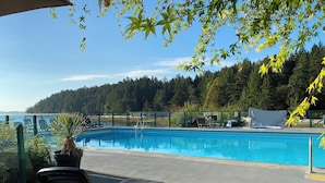 A swimming pool with lounge chairs and a view of the forest and water. - INN OF THE SEA - Stunning views~ Oceanfront Pool & Hot Tub, Private Dock (Ladysmith)