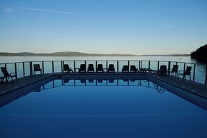 Una piscina con sillas de descanso frente a un lago, rodeada por una barandilla.
