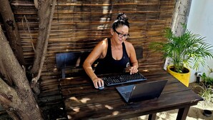 A person sitting at a wooden table outdoors, using a laptop and a keyboard. - Ocean/Beachfront Living ~Rustic Fishing Village w/Upscale Amenities HAVE IT ALL! (El Gigante (Playa Gigante), Tola)
