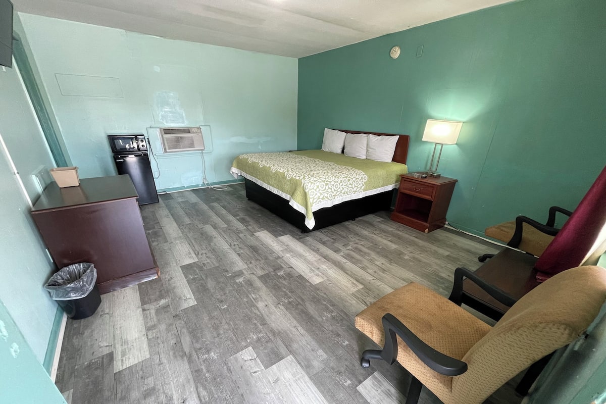 A hotel room with a bed, a desk, a chair, a lamp, and a trash bin.