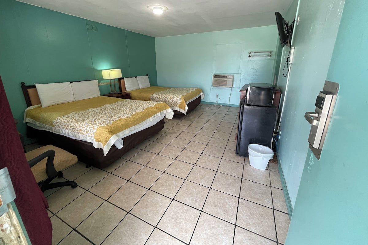 A hotel room with two beds, a desk, a chair, a television, and a refrigerator.