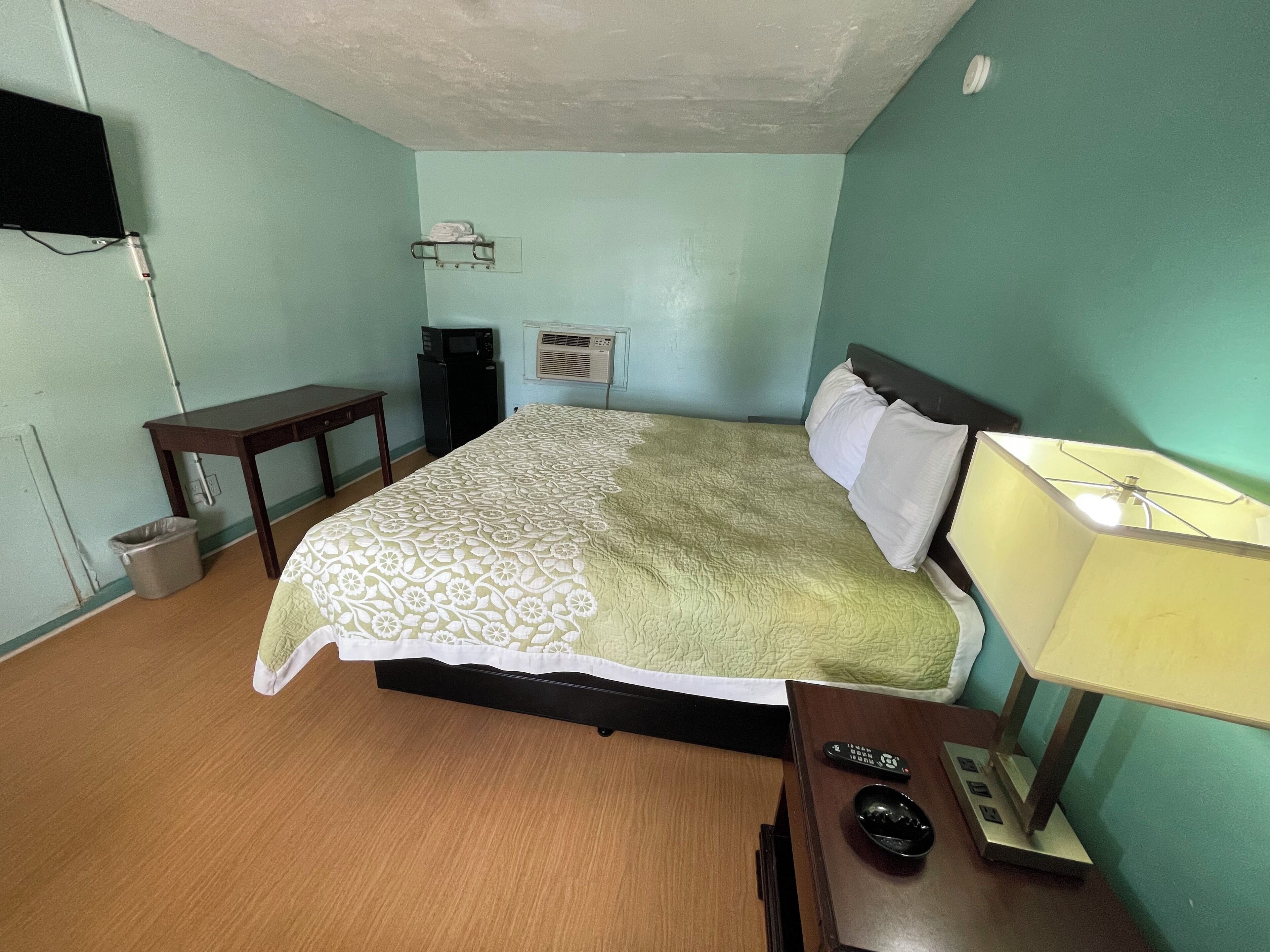 A bedroom with a bed, bedside table, lamp, TV, and a small desk.