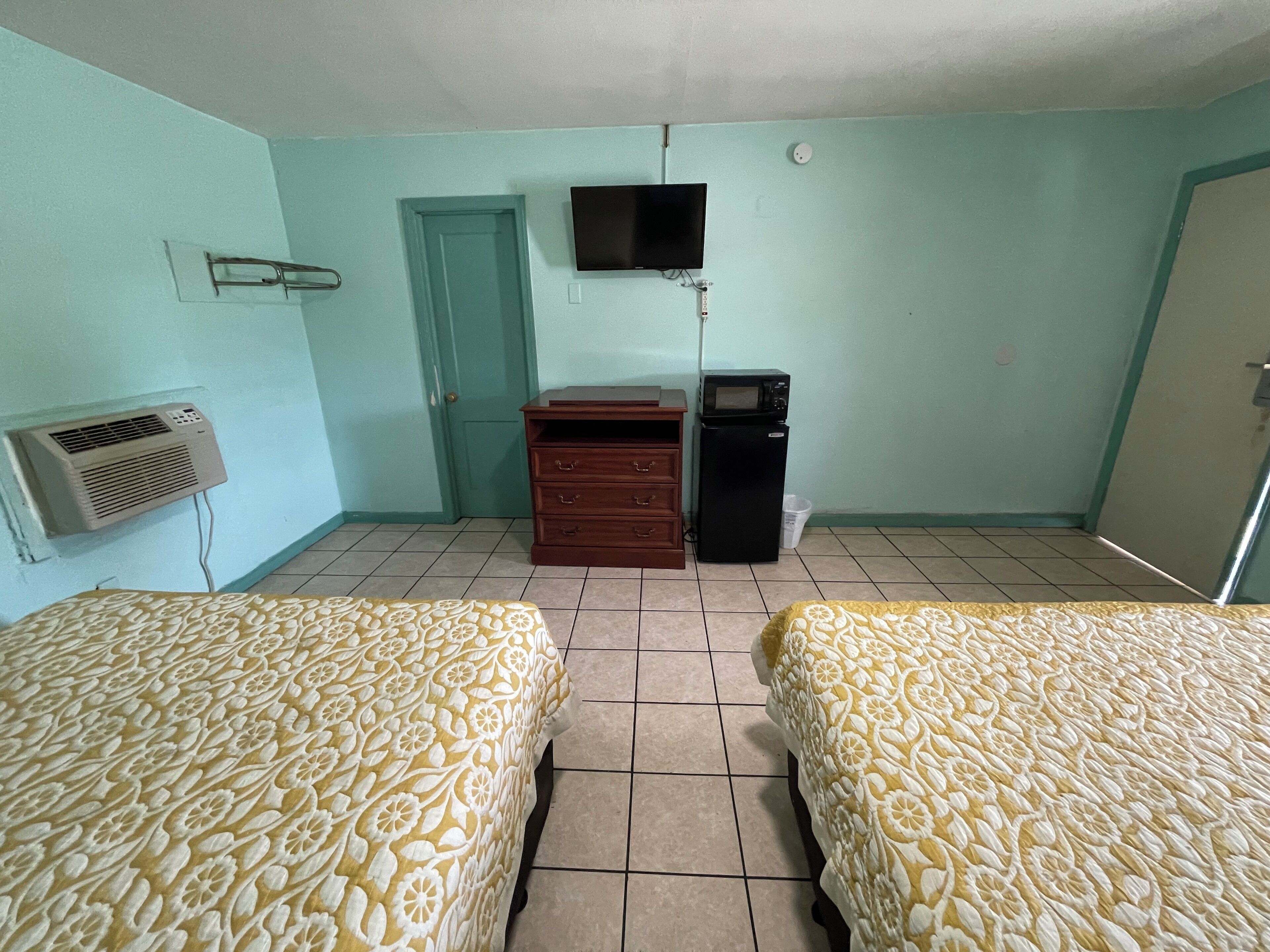 Een kamer met twee bedden, een televisie, een dressoir, een magnetron en een airconditioner.