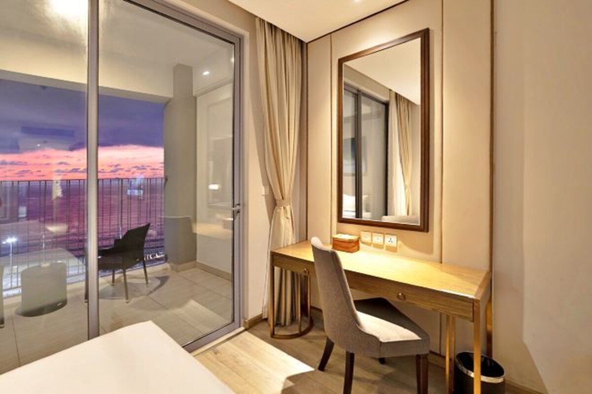 A hotel room with a desk, chair, and a large window with a view of a balcony.