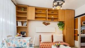 Un espacio habitable compacto con una mesa de comedor, sillas, un sofá, una pequeña mesa de centro y una zona de cocina.