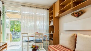 Una sala de estar acogedora con un sofá a cuadros, una mesa de centro con un control remoto, y un comedor con sillas y una mesa.