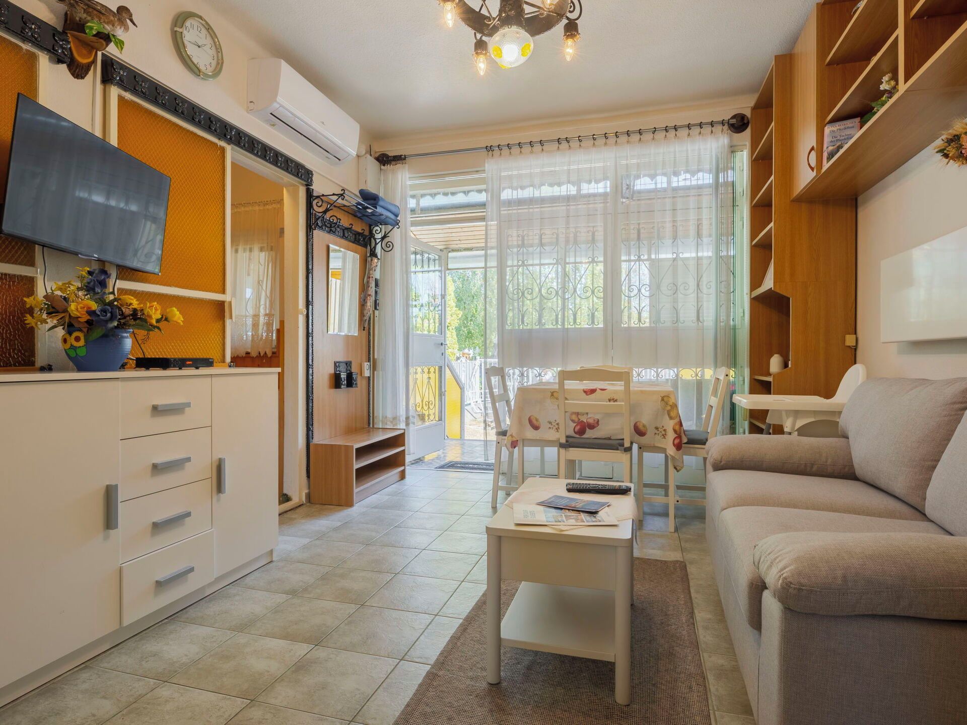 Un saló ben il·luminat amb un sofà, una taula de dinar amb cadires, un televisor i una cuina amb armaris i fogó.